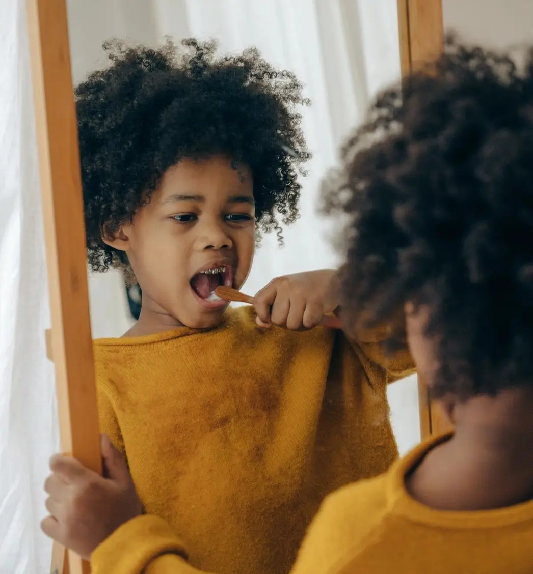 A young child brushing her teeth in front of the mirror.
